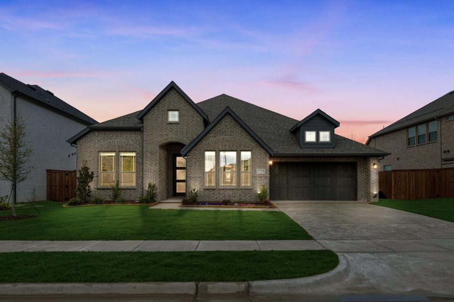 Single-story brick home with two-car garage, arched entry, and green front lawn at dusk