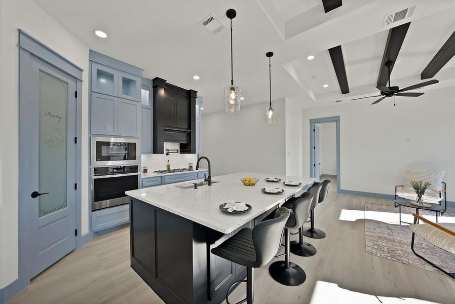 Kitchen with glass insert cabinets, a kitchen bar, decorative light fixtures, stainless steel appliances, and light stone counters
