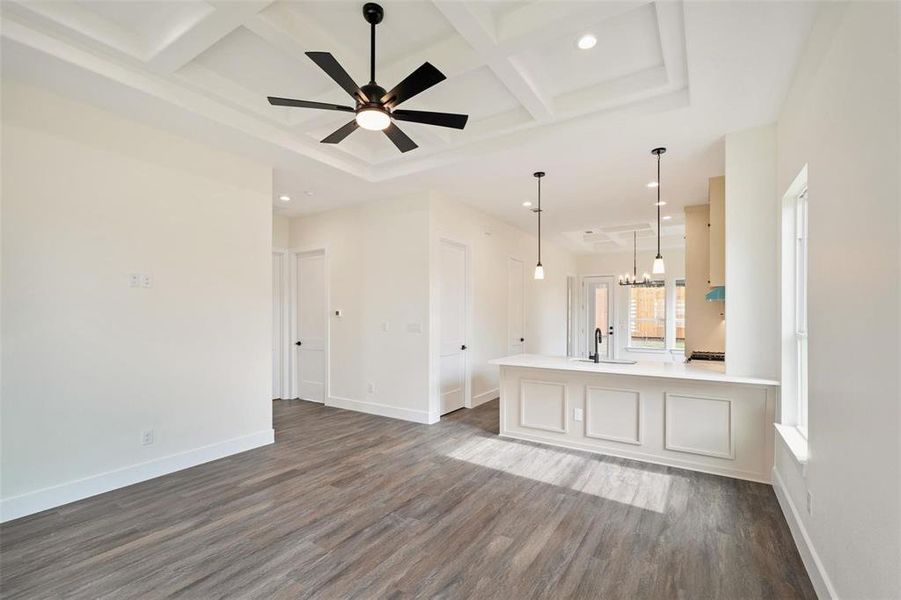 Unfurnished living room with a ceiling fan, coffered ceiling, dark wood finished floors, and hanging lights