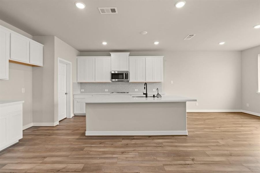 This light and bright kitchen features a large quartz island, white cabinets, a large sink overlooking your family room, recessed lighting, and beautiful backsplash.