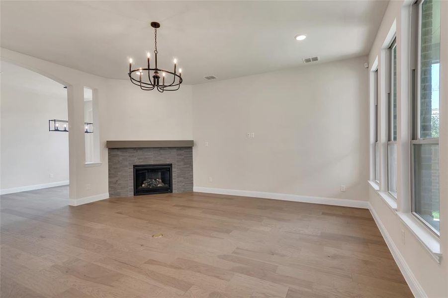 Unfurnished living room with a chandelier, a stone fireplace, light hardwood / wood-style floors, and a wealth of natural light