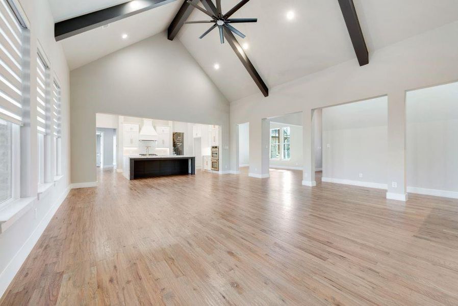 Unfurnished living room featuring ceiling fan, light hardwood / wood-style flooring, high vaulted ceiling, and beamed ceiling