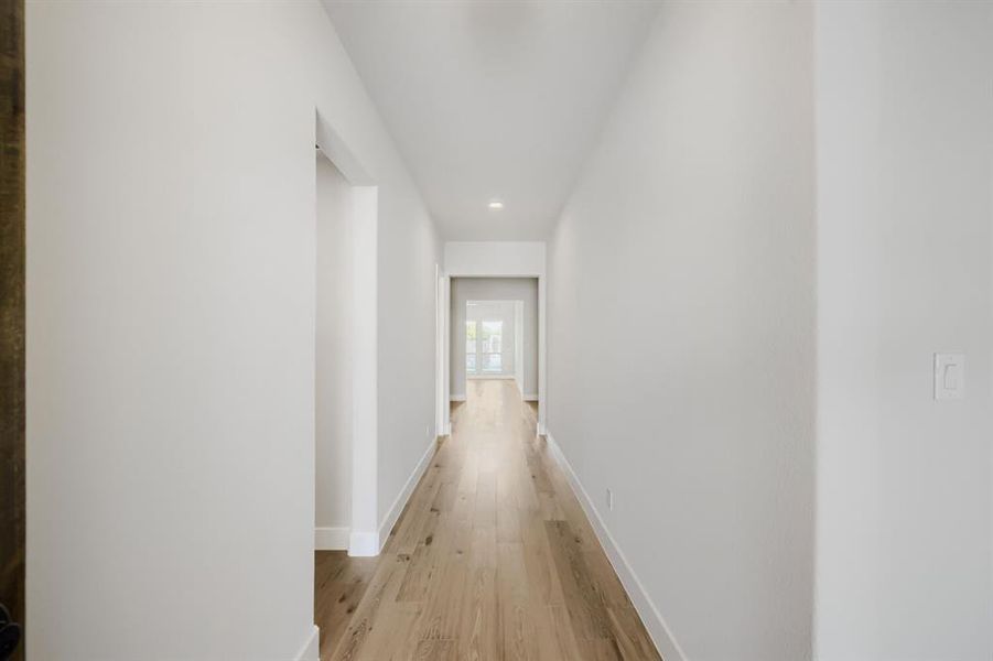 Hallway featuring light wood-finish flooring, white baseboards, recessed lighting, and a neutral wall palette
