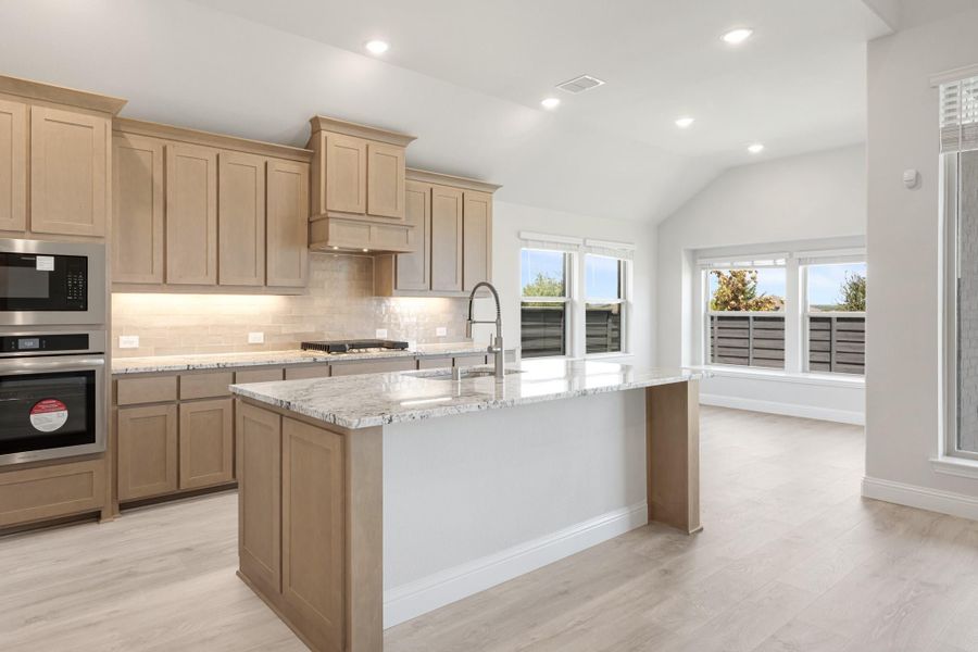 Kitchen with light wood cabinets, granite island, stainless steel appliances, and light hardwood floors