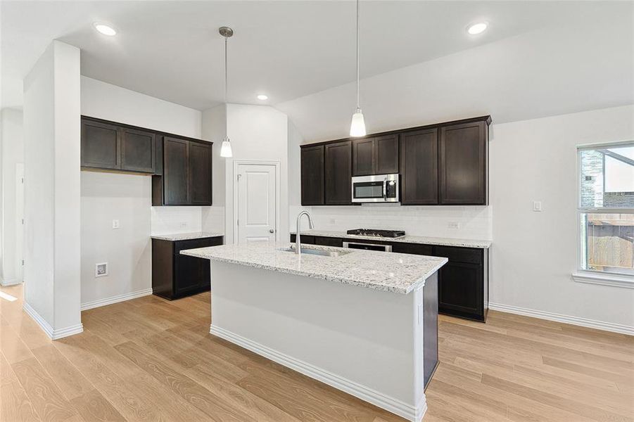 Kitchen featuring sink, hanging light fixtures, backsplash, dark brown cabinetry, and light wood-type flooring