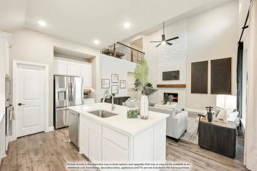 Open-concept kitchen and living area with white island, stainless appliances, stone fireplace, and two-story ceiling