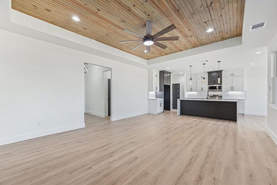 Unfurnished living room featuring light hardwood / wood-style floors, a raised ceiling, and wooden ceiling