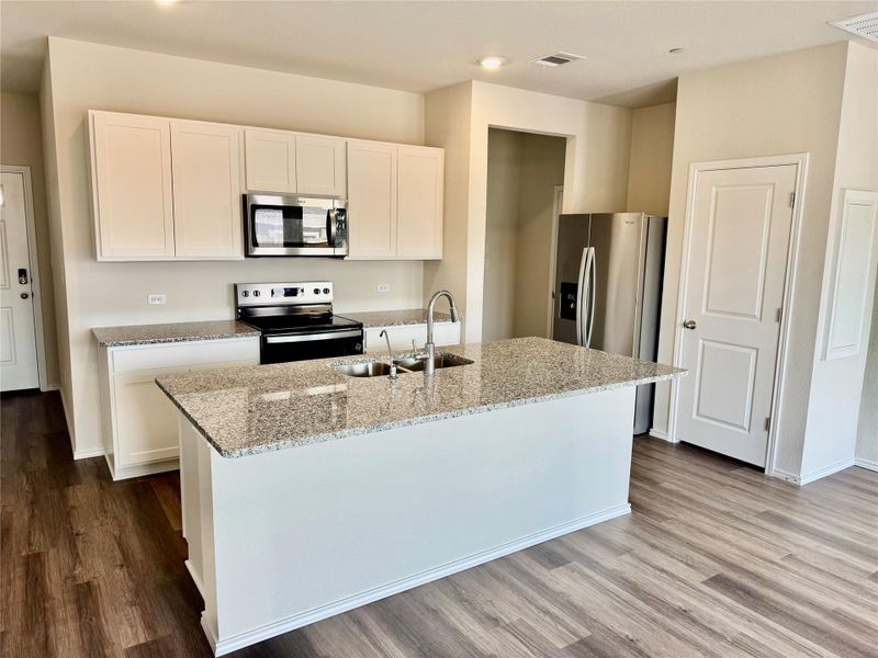 Kitchen featuring appliances with stainless steel finishes, light stone countertops, white cabinets, a kitchen island with sink, and wood finished floors Kitchen featuring appliances with stainless steel finishes, light stone countertops, white cabinets, a kitchen island with sink, and wood finished floors