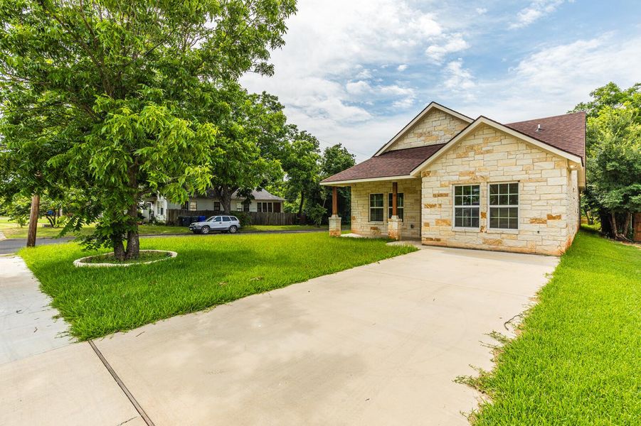 View of front of home featuring stone siding, a front yard, driveway, and a shingled roof