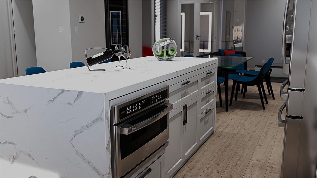 This modern kitchen features a large marble island with integrated appliances, sleek cabinetry, and a bright, open dining area with contemporary furnishings on a stylish wood floor.