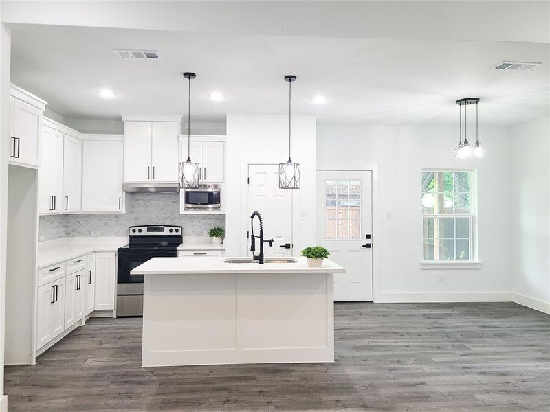 Kitchen featuring stainless steel appliances, under cabinet range hood, decorative backsplash, light countertops, and wood finished floors Kitchen featuring stainless steel appliances, under cabinet range hood, decorative backsplash, light countertops, and wood finished floors