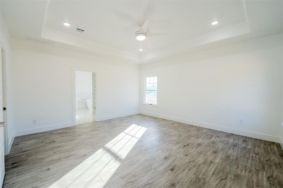Unfurnished room featuring light wood-type flooring, a raised ceiling, recessed lighting, ceiling fan, and ornamental molding Unfurnished room featuring light wood-type flooring, a raised ceiling, recessed lighting, ceiling fan, and ornamental molding