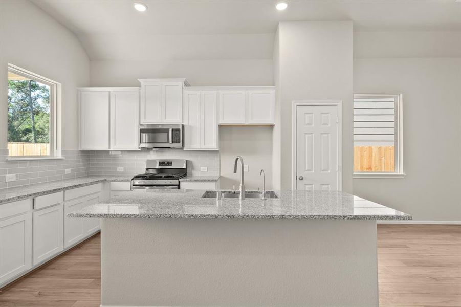 This light and bright kitchen features a large quartz island, white cabinets, a large sink overlooking your family room, recessed lighting, and beautiful backsplash.