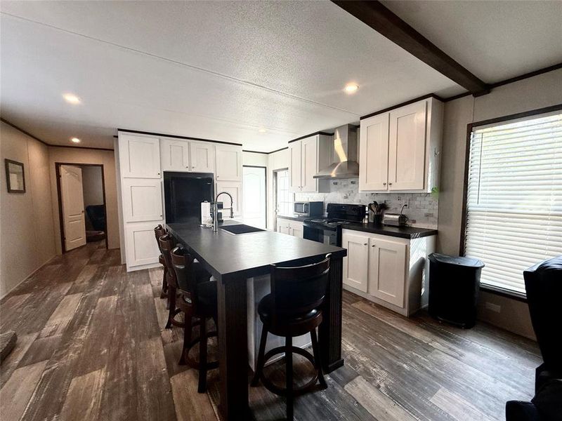 Kitchen featuring dark countertops, decorative backsplash, dark wood-style flooring, white cabinetry, and healthy amount of natural light
