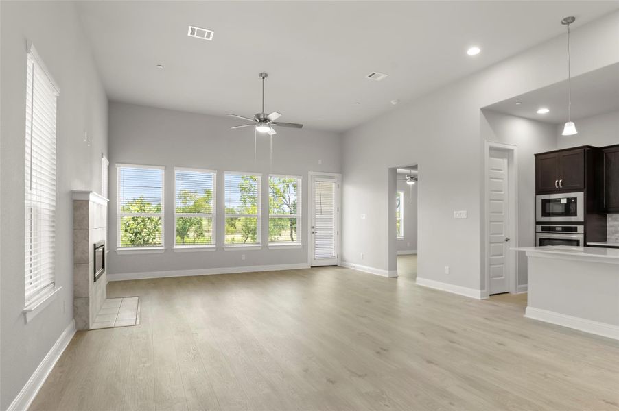 Unfurnished living room featuring ceiling fan, a tiled fireplace, light wood-style flooring, recessed lighting, and a towering ceiling Unfurnished living room featuring ceiling fan, a tiled fireplace, light wood-style flooring, recessed lighting, and a towering ceiling