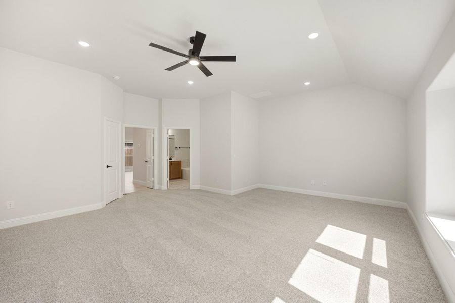 Spacious empty bedroom with beige carpet, black ceiling fan, recessed lighting, and open ensuite bathroom door.