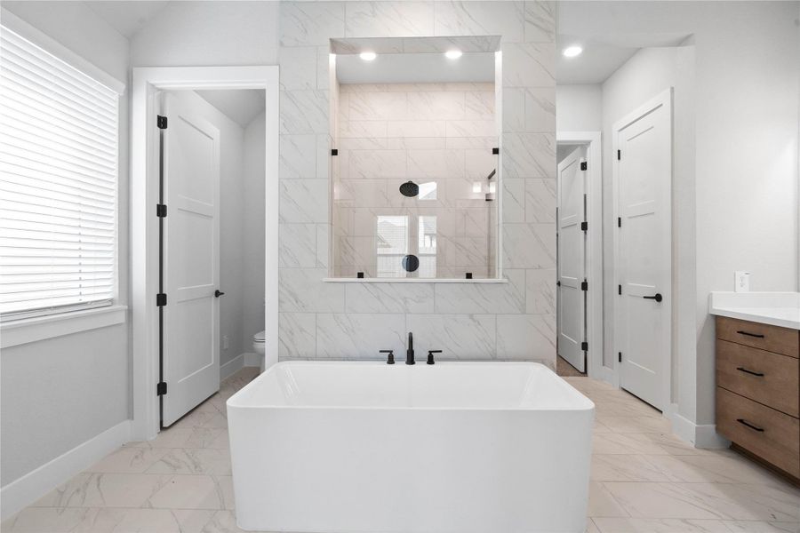 This alternate view of the primary bathroom showcases a large soaking tub perfect for unwinding after a long day, walk-in shower with a stylish tile surround, large walk-in closet, and toilet compartment.