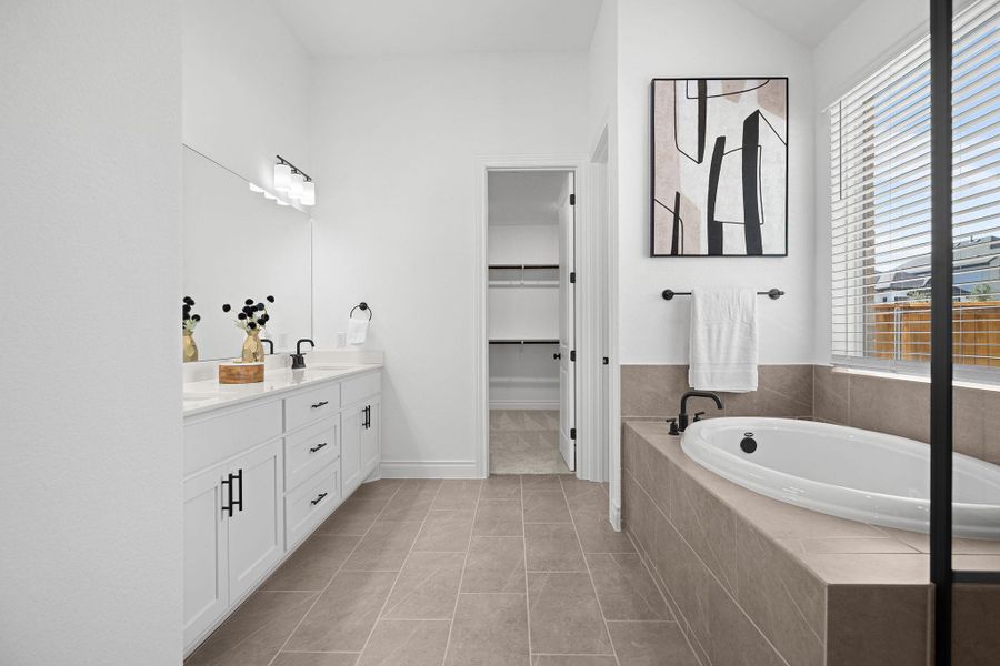 Full bathroom with double vanity, a bath, a walk in closet, and light tile patterned floors