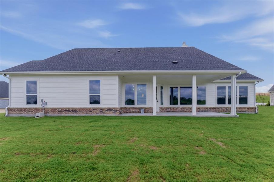 Expansive rear exterior featuring a covered patio with white columns, large windows, white siding, and a brick foundation