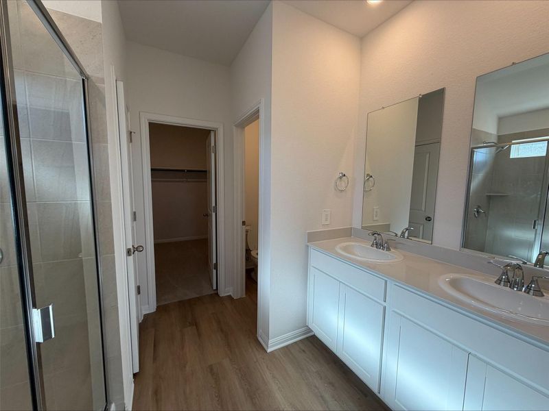 Bathroom featuring a stall shower, a spacious closet, double vanity, and light wood-type flooring