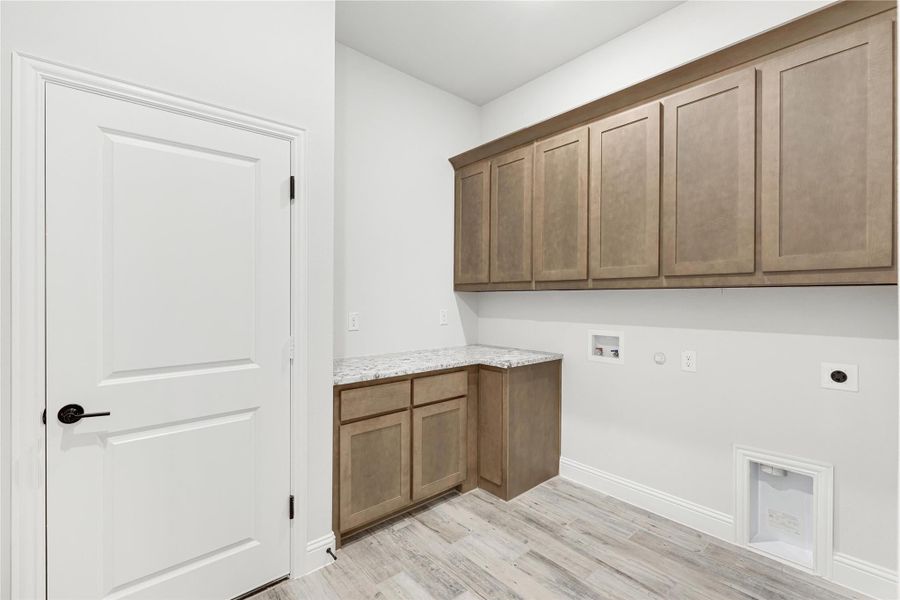 Laundry room with tan wood cabinets, granite countertop, washer hookups, and a pet door on light wood floors.