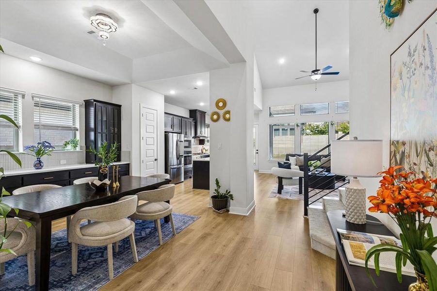 Open-concept interior featuring wood-finish flooring, a modern kitchen with stainless steel appliances, a dining area with a contemporary chandelier, and a living space with vaulted ceilings and large windows Open-concept interior featuring wood-finish flooring, a modern kitchen with stainless steel appliances, a dining area with a contemporary chandelier, and a living space with vaulted ceilings and large windows