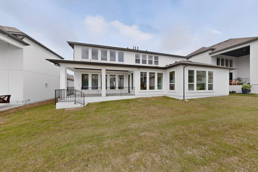 Contemporary architecture featuring a white exterior, multiple large windows, and a covered patio with black railings