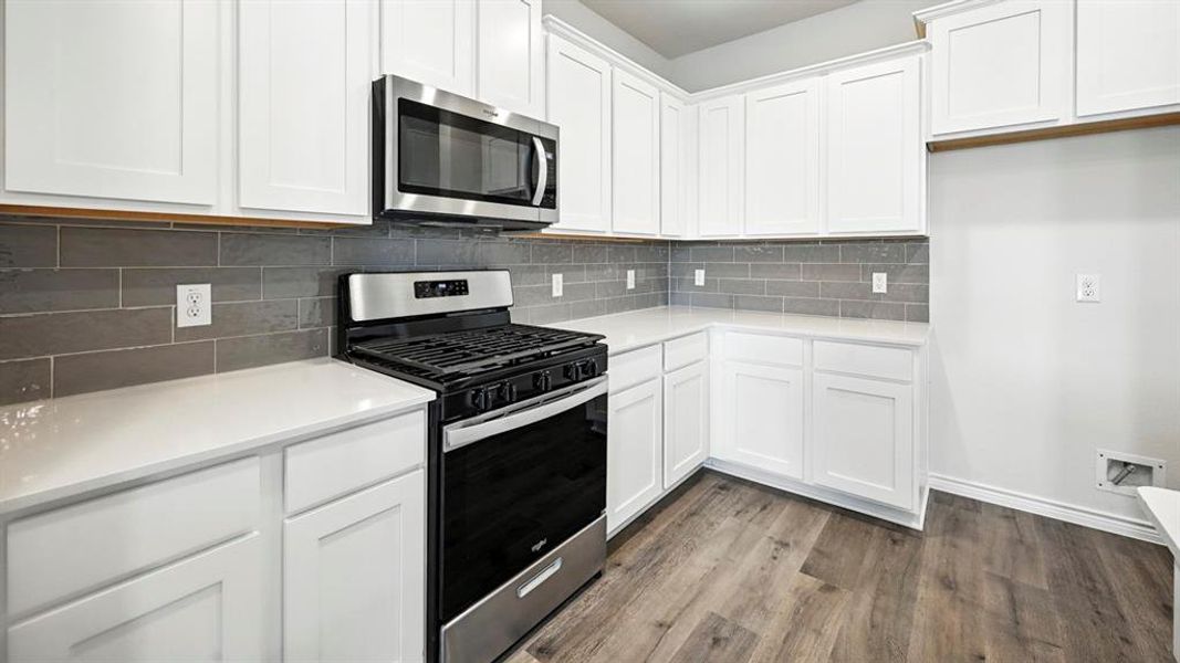 Kitchen featuring white cabinetry, light-toned countertops, a stainless steel microwave, a stainless steel and black range, and gray subway tile backsplash