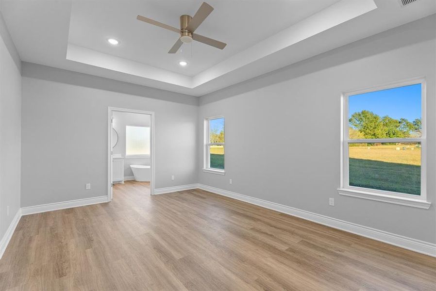 Unfurnished bedroom featuring a raised ceiling, ceiling fan, light wood-style floors, and recessed lighting