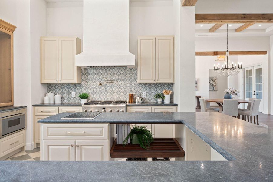 Kitchen with cream cabinetry, decorative backsplash, custom exhaust hood, beam ceiling, and dark stone counters