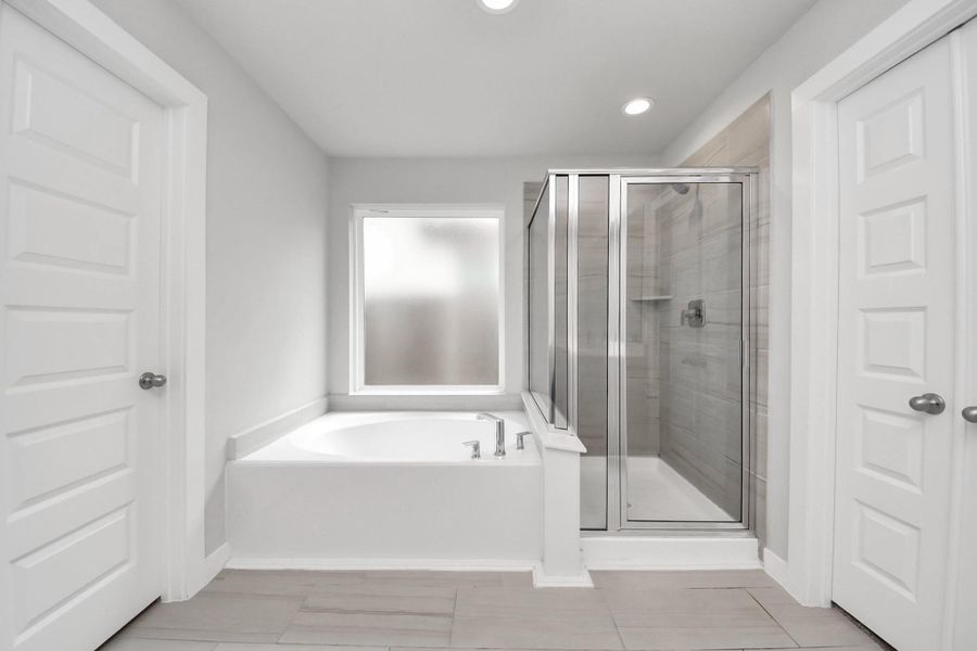 Spa-like primary bathroom featuring a relaxing soaking tub positioned beneath a frosted window for privacy and natural light, alongside a separate glass-enclosed walk-in shower with modern tile surround.