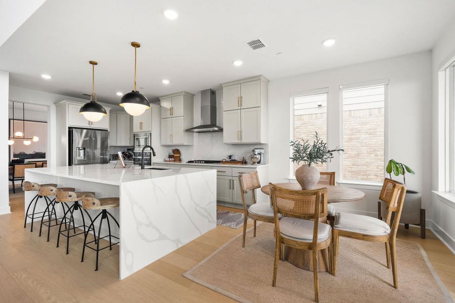 Modern kitchen featuring light wood-finish flooring, recessed lighting, and a large central island with a waterfall countertop Modern kitchen featuring light wood-finish flooring, recessed lighting, and a large central island with a waterfall countertop