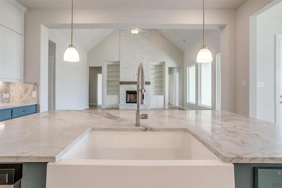 Kitchen featuring a stone fireplace, tasteful backsplash, decorative light fixtures, and sink