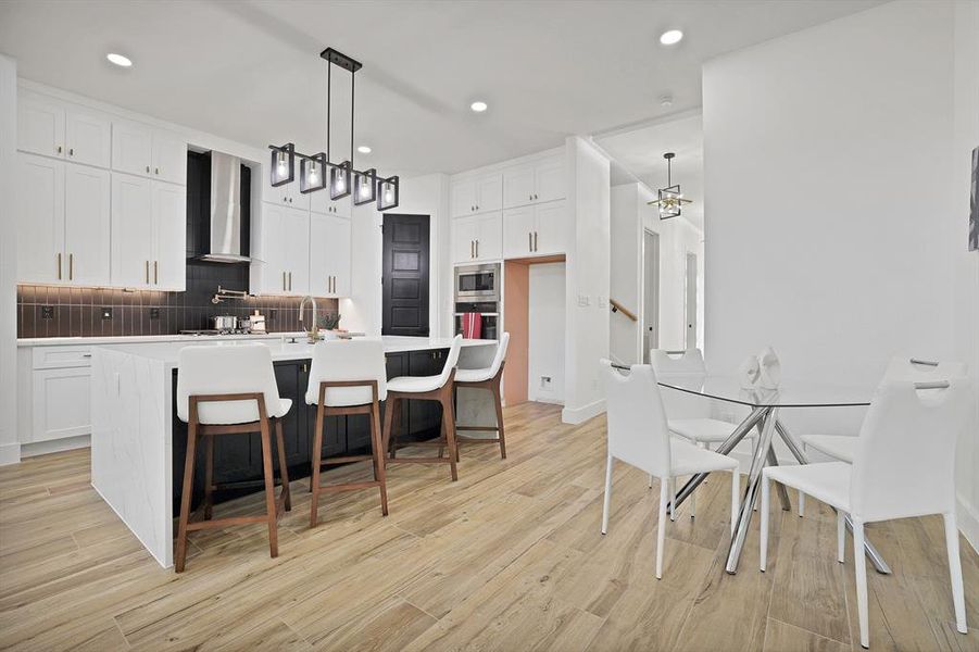 Kitchen with appliances with stainless steel finishes, white cabinetry, light hardwood / wood-style flooring, and wall chimney range hood