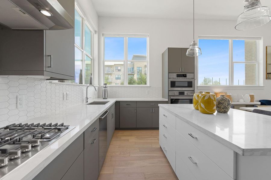 Kitchen with gray cabinetry, ventilation hood, stainless steel appliances, light wood finished floors, and decorative light fixtures