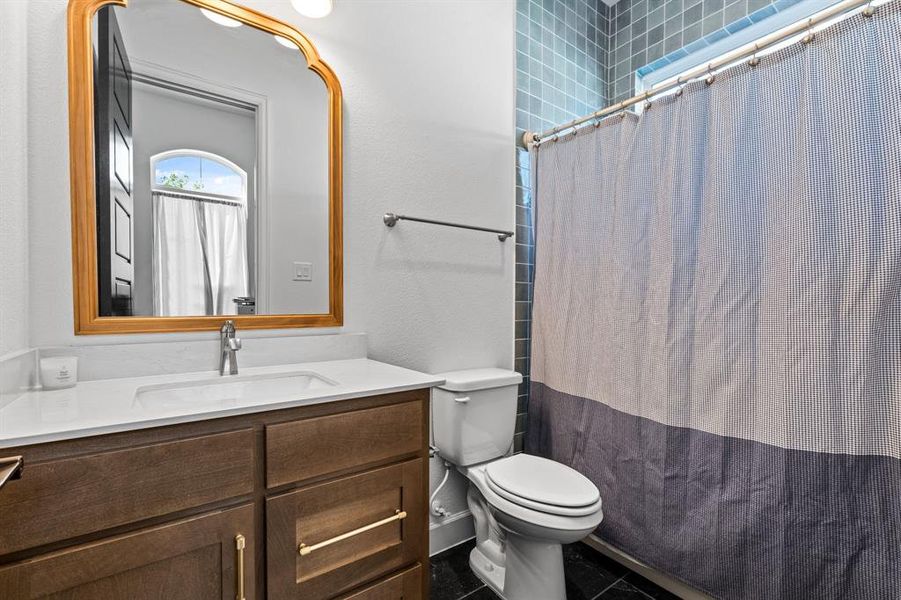 Bathroom featuring vanity, a shower with curtain, dark tile patterned floors, and a textured wall Bathroom featuring vanity, a shower with curtain, dark tile patterned floors, and a textured wall