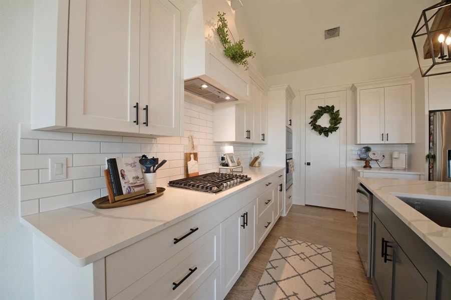 Kitchen with white cabinetry, backsplash, light stone countertops, and light wood-style floors