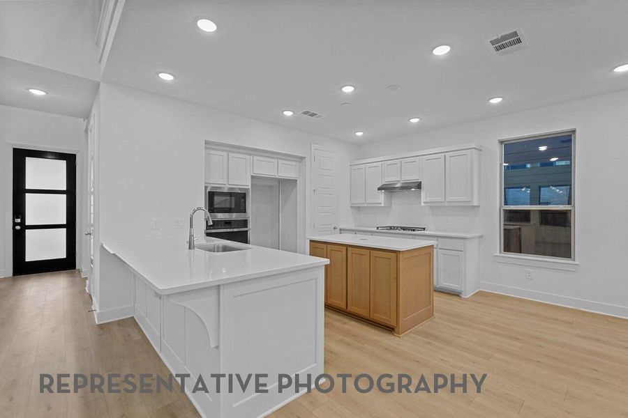 A bright, inviting kitchen features a central island, crisp white cabinetry, large windows, and abundant lighting that fills the space with warmth and clarity.