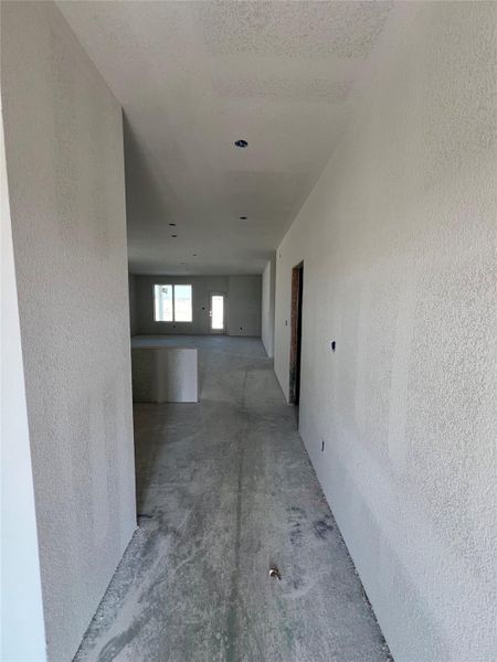 Hall featuring a textured wall, a textured ceiling, and concrete floors