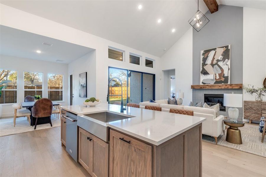 Kitchen with light wood-style floors, a glass covered fireplace, light stone countertops, brown cabinetry, and open floor plan Kitchen with light wood-style floors, a glass covered fireplace, light stone countertops, brown cabinetry, and open floor plan