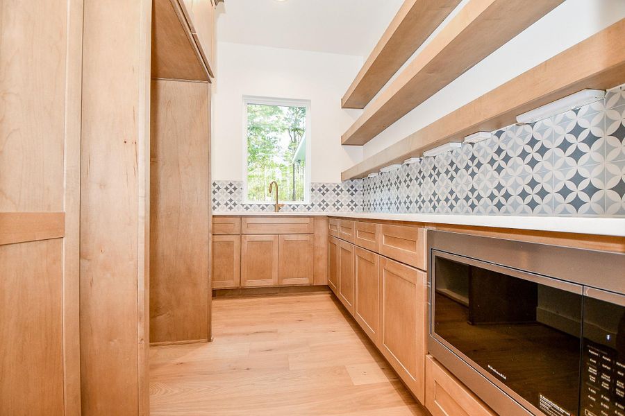 Tucked just behind the main kitchen is an impressive prep space with natural wood cabinetry, designer tile backsplash, open shelving, and a dedicated microwave and sink area. Ideal for hosting, meal prep, or extra storage. Tucked just behind the main kitchen is an impressive prep space with natural wood cabinetry, designer tile backsplash, open shelving, and a dedicated microwave and sink area. Ideal for hosting, meal prep, or extra storage.