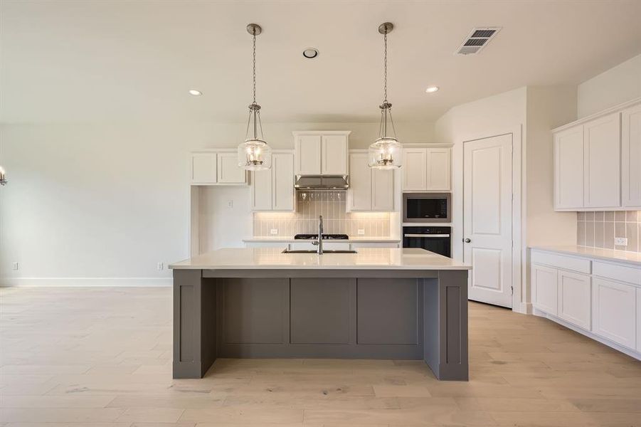Kitchen with dual tone cabinetry, tasteful backsplash, stainless steel appliances, an island with sink, and light wood finished floors