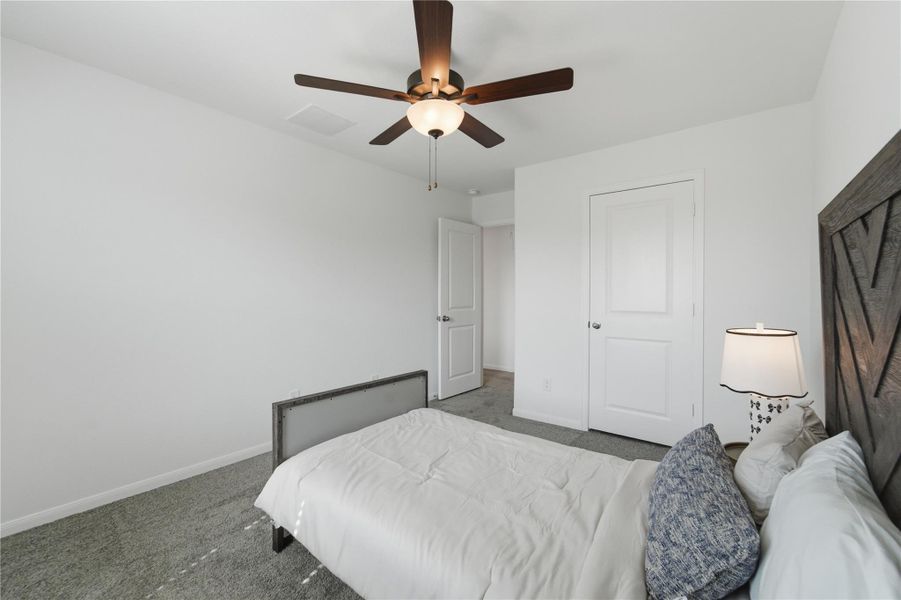 A well-lit bedroom features plush carpeting and a modern ceiling fan, offering comfortable living. A well-lit bedroom features plush carpeting and a modern ceiling fan, offering comfortable living.
