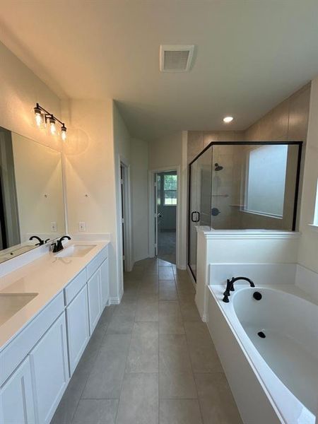 Bathroom featuring a double vanity with white cabinetry and integrated sinks, a freestanding soaking tub with matte black fixtures, a walk-in shower with a glass enclosure, and light-toned tile flooring