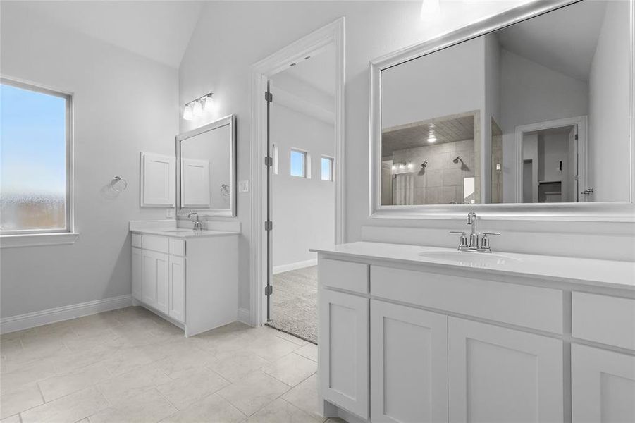 Bathroom with lofted ceiling, tiled shower, two vanities, and baseboards Bathroom with lofted ceiling, tiled shower, two vanities, and baseboards