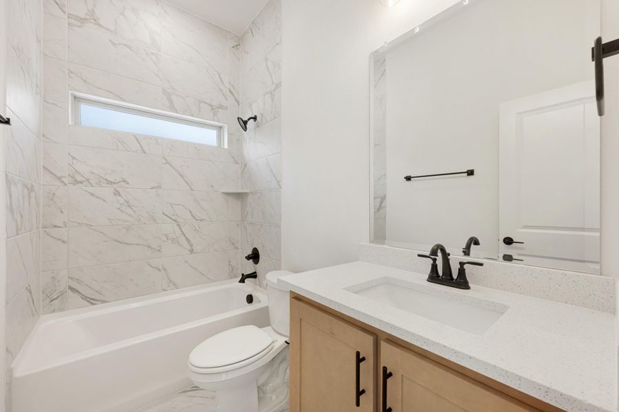 Bathroom with marble-look tile tub surround, white quartz vanity, and matte black fixtures