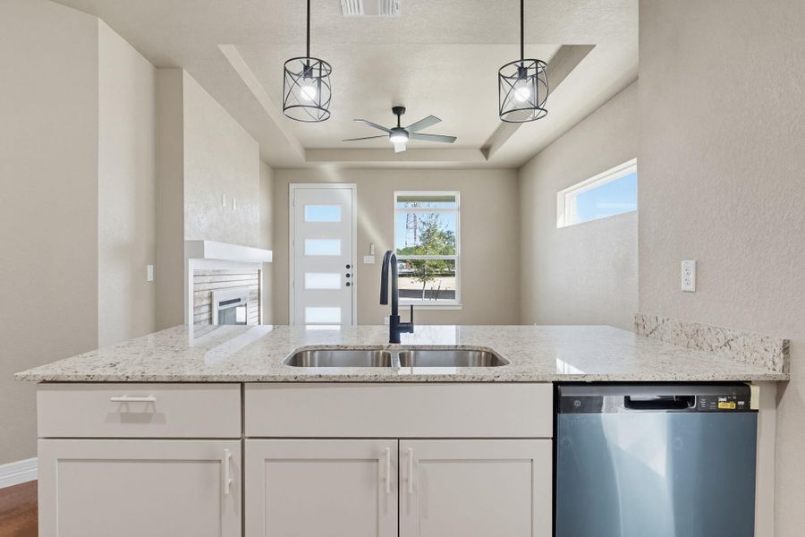 Kitchen with a tray ceiling, stainless steel dishwasher, light stone countertops, white cabinetry, and a fireplace