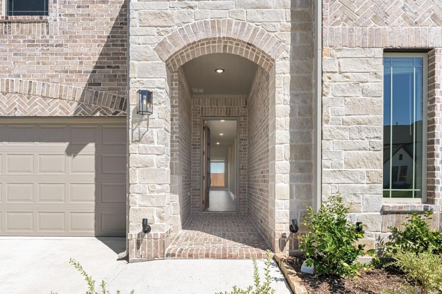 Home entrance with arched brick and stone surround, covered entryway, and attached garage door nearby. Home entrance with arched brick and stone surround, covered entryway, and attached garage door nearby.