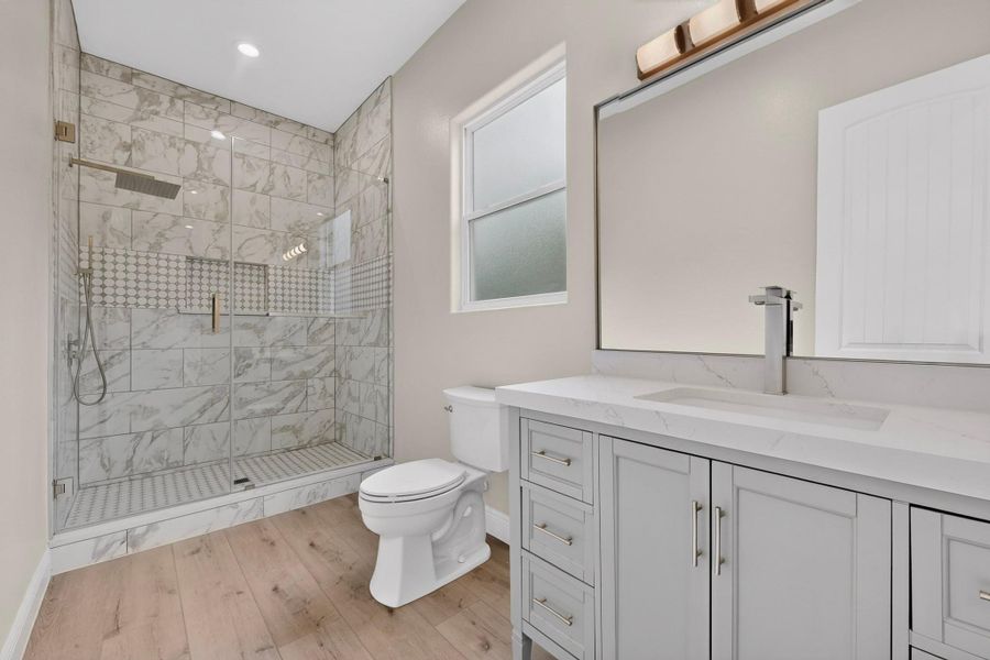 Plank flooring pairs with a glass-enclosed walk-in shower featuring custom stone tilework.