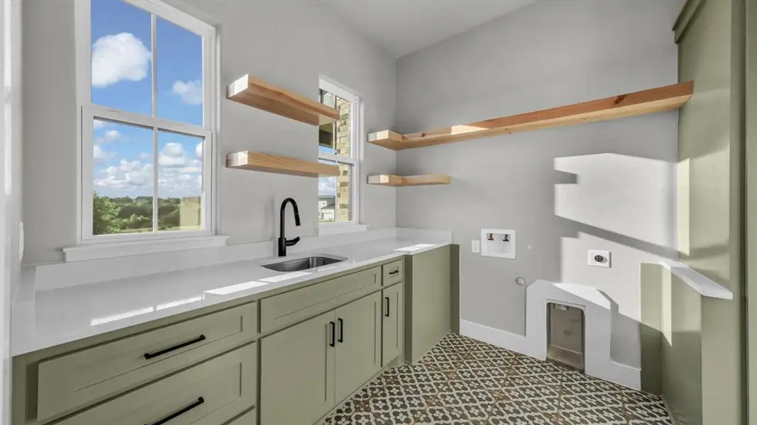 Utility room featuring sage green cabinetry, white countertops, stainless steel sink with matte black faucet, and patterned floor tiling Utility room featuring sage green cabinetry, white countertops, stainless steel sink with matte black faucet, and patterned floor tiling